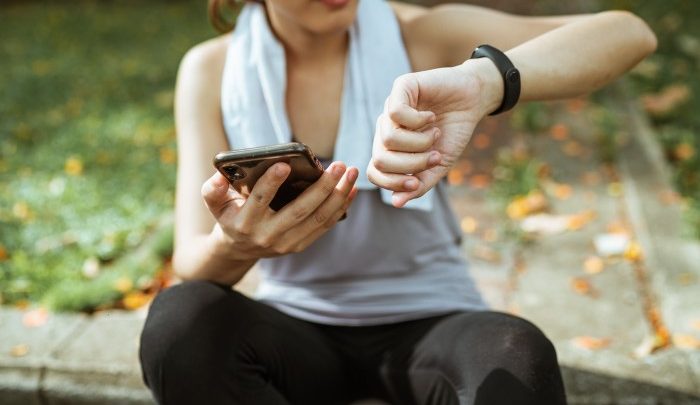 Woman in exercise clothes looking at her watch and holding a phone