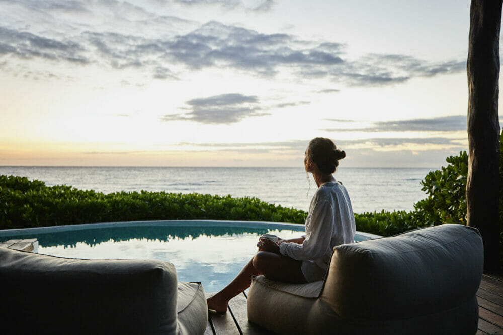 Wide_shot_of _woman_watching_sunrise_while_sitting_poolside_at_luxury_suite_at_tropical_resort.