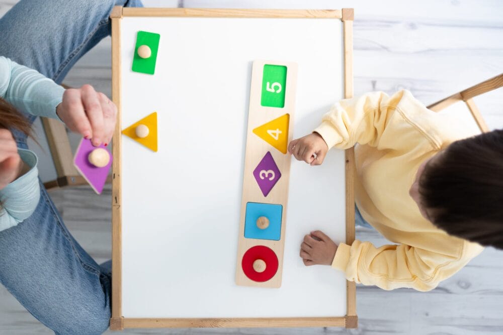 Top-view-of-a-female-therapist-and-autistic-boy-playing-skill-games-in-nursery